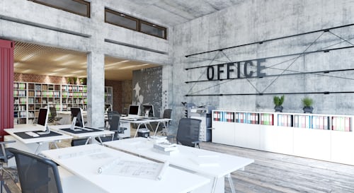 Modern open-concept office with industrial-style concrete walls, white desks, ergonomic chairs, and organized shelving filled with colorful binders. The space features natural lighting and a large wall sign that reads “OFFICE.